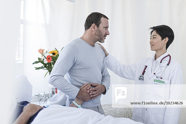 Doctor consoling man visiting patient in hospital