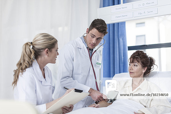 Arzt und Krankenschwester untersuchende Frau im Krankenhausbett