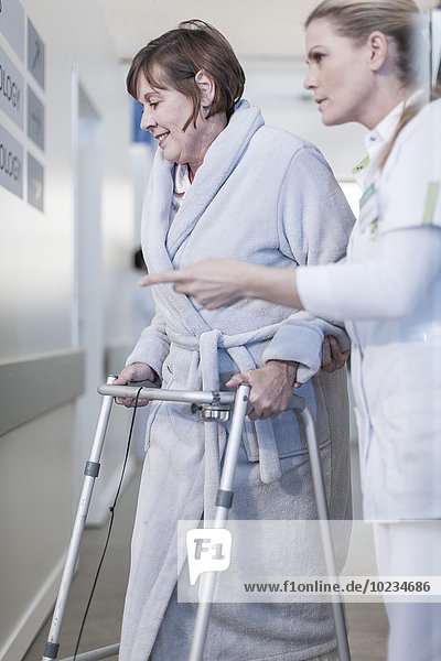 Nurse helping patient with walking frame in hospital corridor