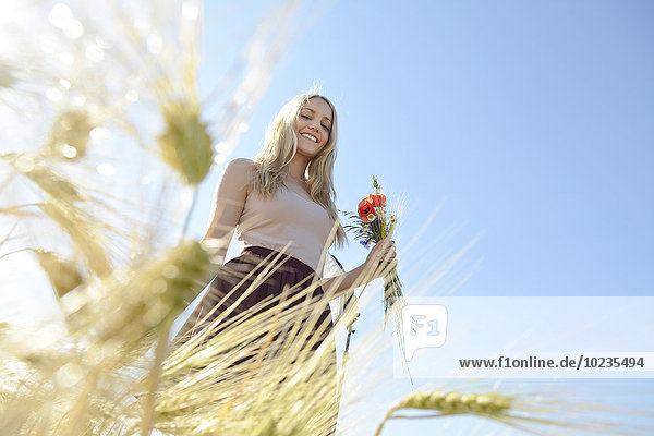 Lächelnde junge Frau mit einem Strauß Feldblumen  die auf einem Roggenfeld stehen.