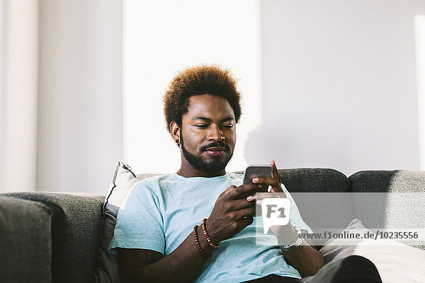 Junger Mann zu Hause beim Lesen von Nachrichten auf dem Smartphone