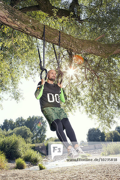 Mann bei der CrossFit-Übung an Ringen  die am Baumstamm hängen