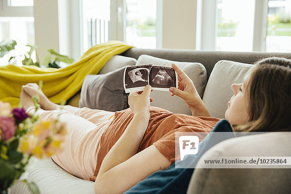 Schwangere schaut auf die Ultraschalluntersuchung  während sie sich auf der Couch entspannt.