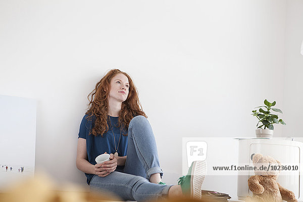 Daydreaming young woman sitting on floor of her living room
