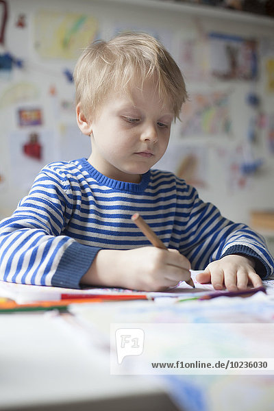 Portrait of blond little boy painting with crayon