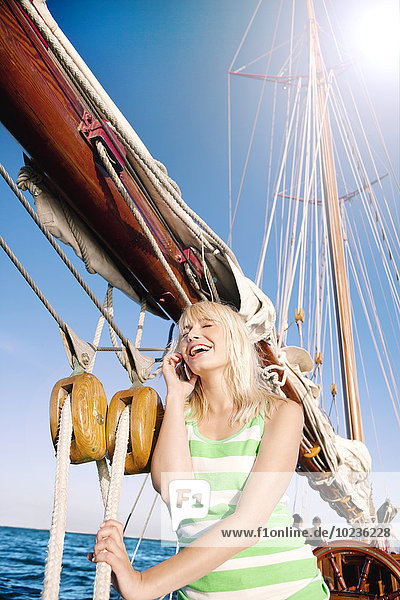 Lachende junge Frau mit Handy auf einem Segelschiff