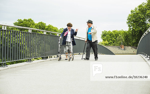 Senior couple with walking stick and wheeled walker on a bridge