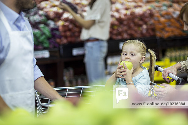 Mädchen sitzt im Einkaufswagen und isst Apfel