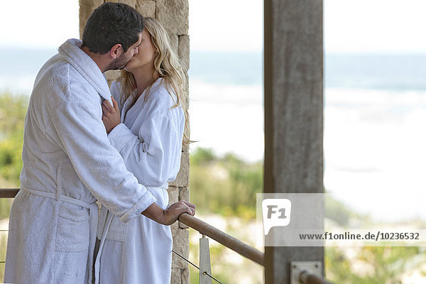 Junges Paar im Bademantel küssend im Strandhaus