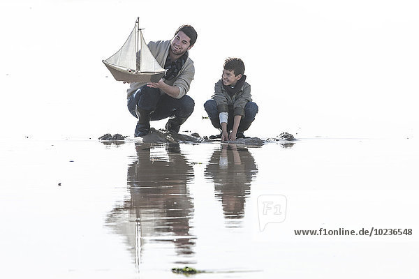 Vater und Sohn mit Spielzeug-Segelboot am Strand