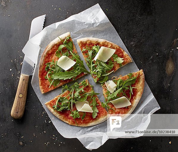 Pizza Margherita mit Rucola und Parmesan auf Papier mit Messer