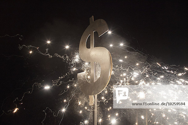 Beleuchtetes Dollarzeichen mit Feuerwerk bei Nacht