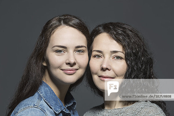 Porträt von lächelnder Mutter und Tochter vor übergrauem Hintergrund