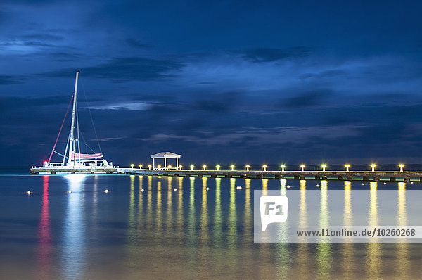 Segelboot am beleuchteten Pier auf dem See gegen den Himmel bei Nacht vertäut