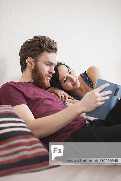 Young man reading book for woman in bed