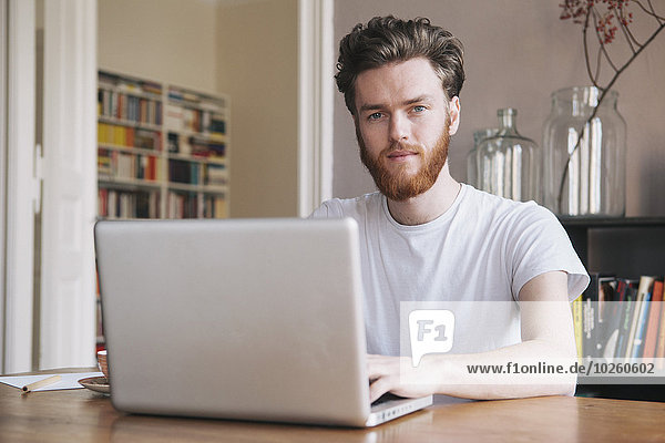 Porträt eines selbstbewussten jungen Mannes mit Laptop am Tisch