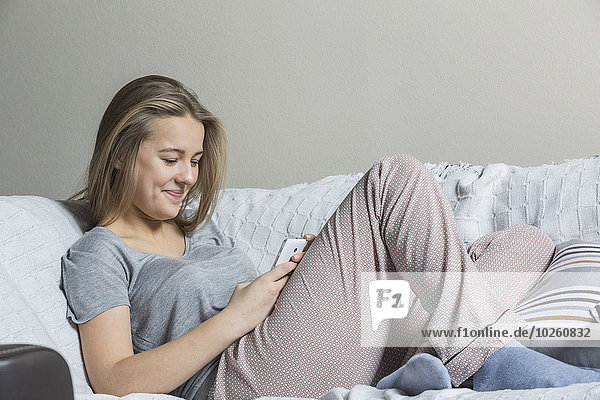 Lächelndes Teenagermädchen mit Smartphone auf dem Sofa zu Hause