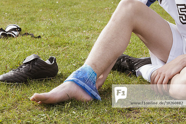 Low section of soccer player applying ice pack on ankle in field