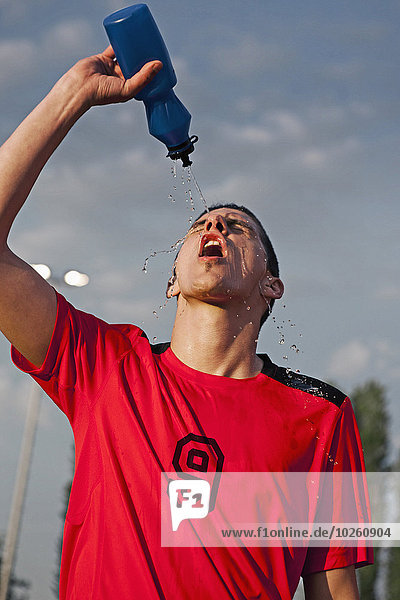 Young male soccer playing squirting water on face
