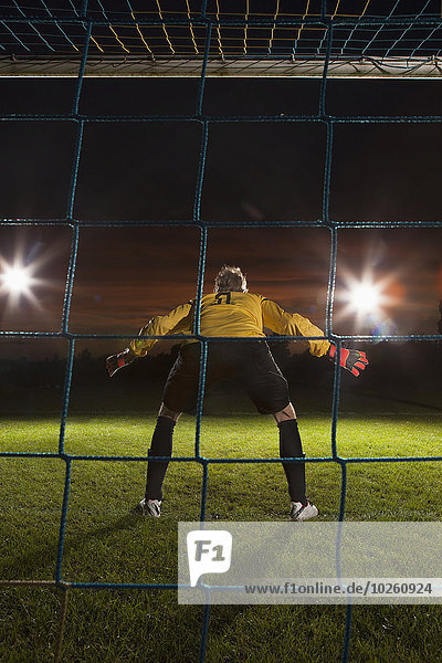 Full length rear view of goalie defending soccer net on field