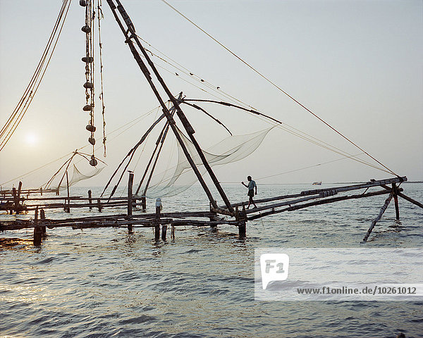 Mitteldistanzansicht eines Mannes der bei Sonnenuntergang auf einem kommerziellen Fischernetz auf See läuft