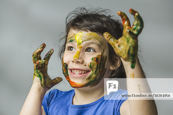 Smiling girl with painted face and hands over gray background