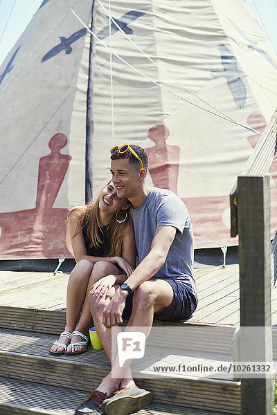 Happy young couple sitting on teepee structure while glamping
