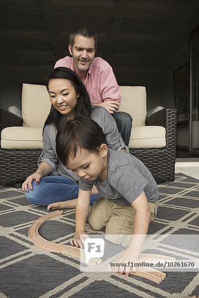 Smiling man and woman playing with their young son  building a wooden railway.
