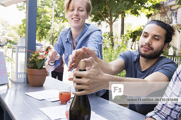 Young man and woman outdoors at a cafe  one trying to recork a bottle of wine.
