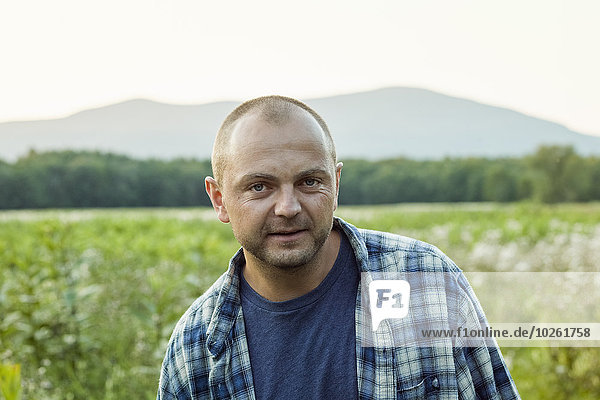 A man outdoors in a wild flower meadow wearing a checked shirt.