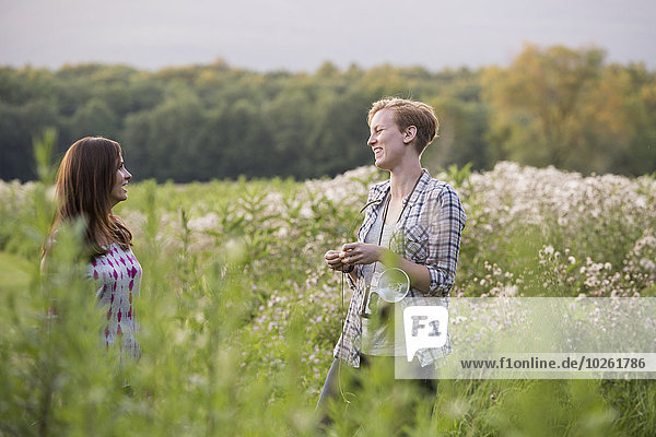 Two women standing in a meadow surrounded by tall grass and wild flowers.