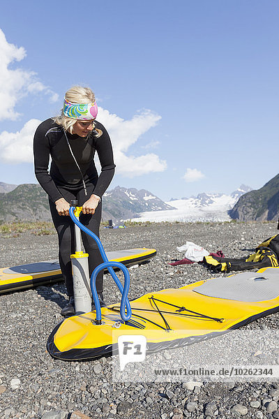 Woman pumps up an inflatable paddle board with Grewingk glacier in the background  Kachemak Bay State Park  Southcentral Alaska.