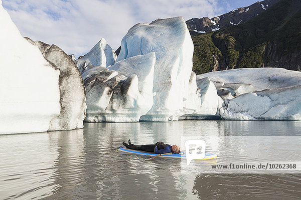 Man laying on a standup paddleboard in front of Grewingk glacier in Kachemak Bay State Park  Southcentral Alaska.