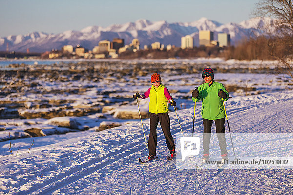 Two people cross country skiing on the Tony Knowles Coastal Trail with Anchorage in the background  Southcentral Alaska