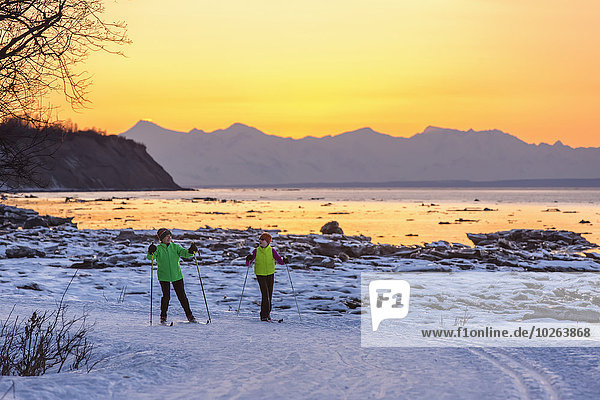 Two back lit people cross country skiing on the Tony Knowles Coastal Trail at sunset  Southcentral Alaska