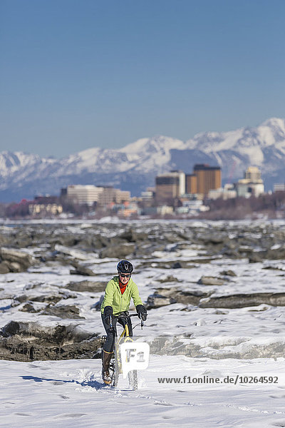 A young woman rides her studded tire bicycle amongst the ice chunks in the Cook Inlet next to the Tony Knowles Coastal Trail  Anchorage  Southcentral Alaska  USA.