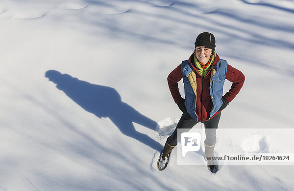 A smiling young woman wearing a hat and gloves stands in a snowbank  Winter  Southcentral Alaska  USA