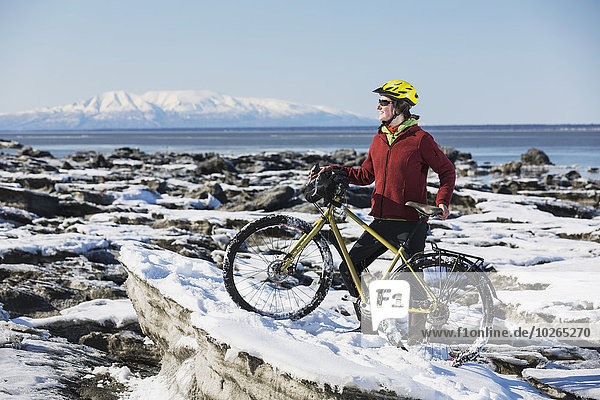Young woman with her bicycle stands on frozen ice chunks along the Tony Knowles Coastal Trail  Anchorage  Southcentral Alaska