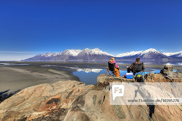 Couple sitting and enjoying the view of the Chugach Mountains along Turnagain Arm near Hope on the Kenai Peninsula  Southcentral Alaska  Spring  HDR