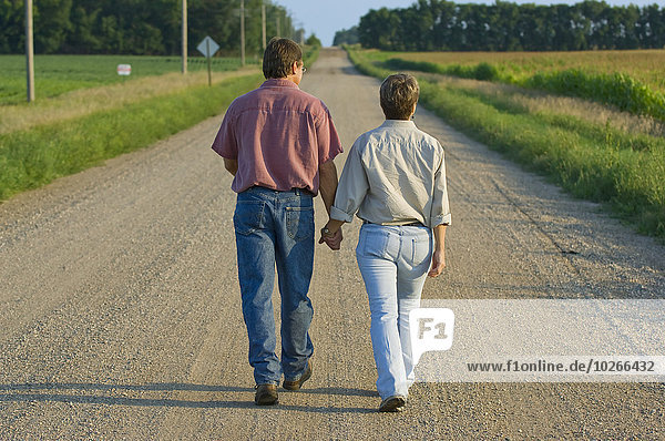Agriculture - Husband and wife farmers walk down a country road hand-in-hand sharing some personal moments together / Minnesota  USA.