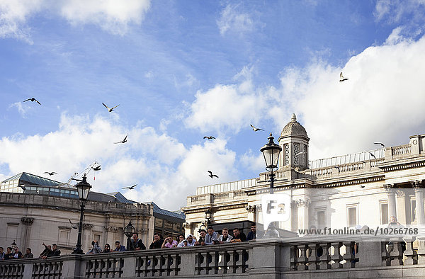 People overlooking Trafalgar Square from the railing in front of The National Gallery; London  England