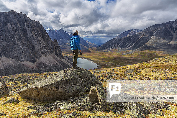Man standing on a rock overlooking the granite peaks of Tombstone Territorial Park in autumn; Yukon  Canada