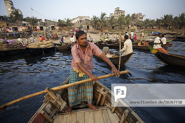 A man stands in a wooden boat rowing with large wooden paddle; Sadarghat  Dhaka  Bangladesh