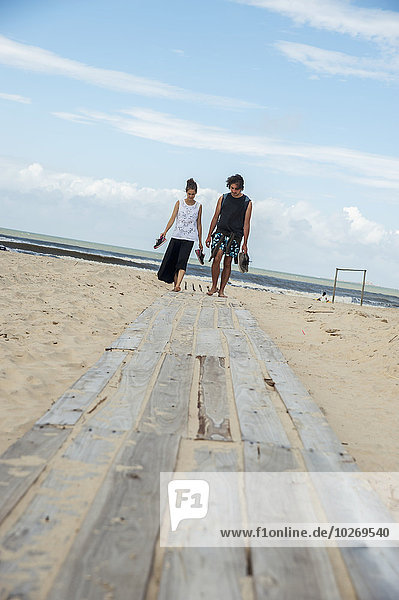A couple walking barefoot along a wooden boardwalk on the beach  Paseo de las Lindas; Valizas  Uruguay