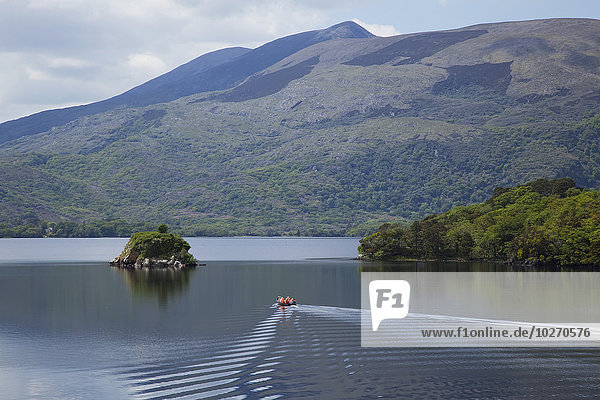 A small boat floats through tranquil water of the Lakes of Killarney surrounded by mountains; Killarney  County Kerry  Ireland