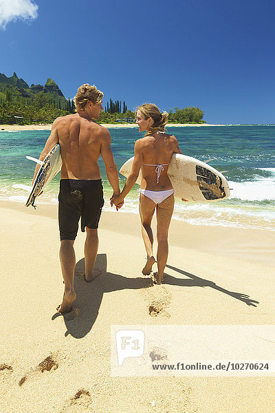 Couple walking on beach with bodyboards; Kauai  Hawaii  United States of America