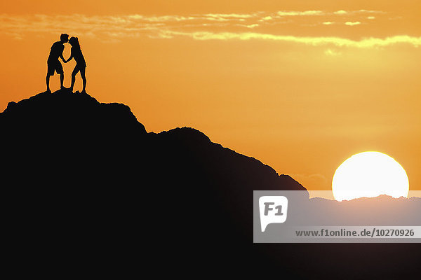Silhouetted couple kissing on a big rock at sunset; Oahu  Hawaii  United States of America