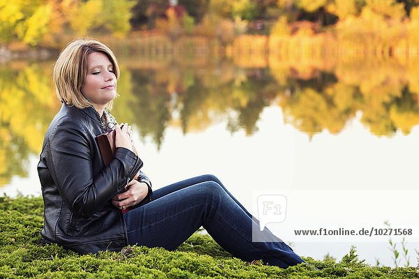 'Mature Christian woman embracing her Bible in a city park beside a lake in autumn; Edmonton  Alberta  Canada'