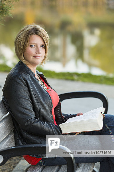 'Mature Christian woman studying her Bible in a city park setting beside a lake; Edmonton  Alberta  Canada'
