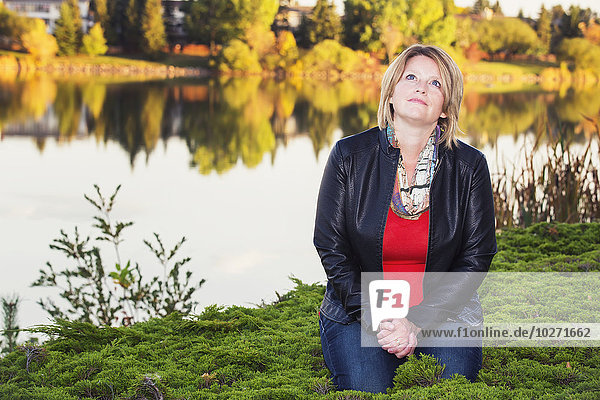 'Mature christian woman kneeling and praying beside lake in autumn; Edmonton  Alberta  Canada'